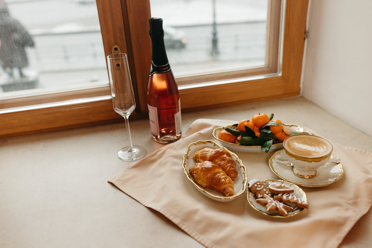 Elegant breakfast with croissants, coffee, and champagne by a window with a winter view.