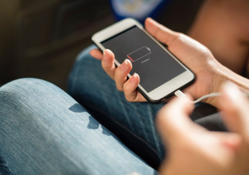 Mano sosteniendo un teléfono inteligente conectado al cargador (imagen ilustrativa)