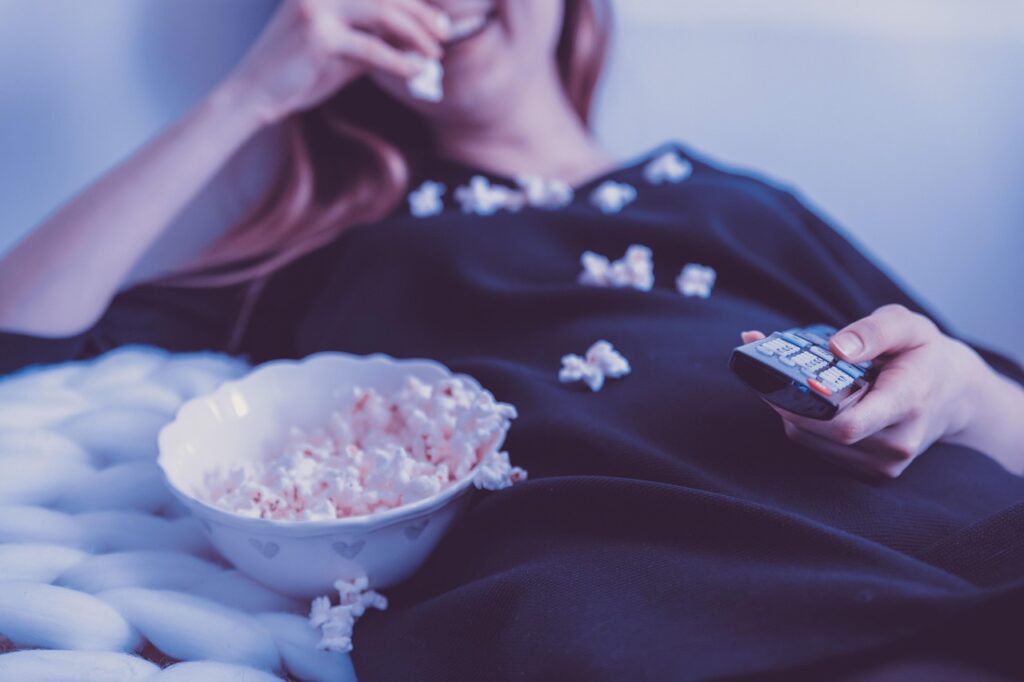 Persona en el sofá viendo una película en la televisión con palomitas