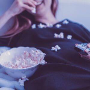 Persona en el sofá viendo una película en la televisión con palomitas