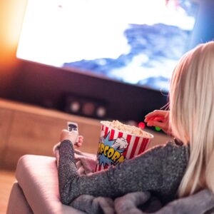 Persona comiendo palomitas mientras ve una película en el televisor